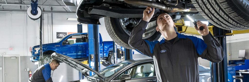 Ford service technicians working under a car in a Ford service center.