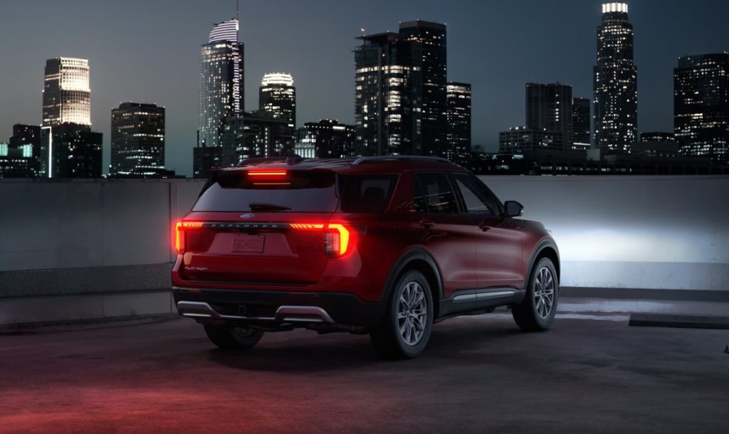 A red Ford Explorer is parked on the top of a parking garage whilst overlooking a city similar to Spartanburg or Greenville.